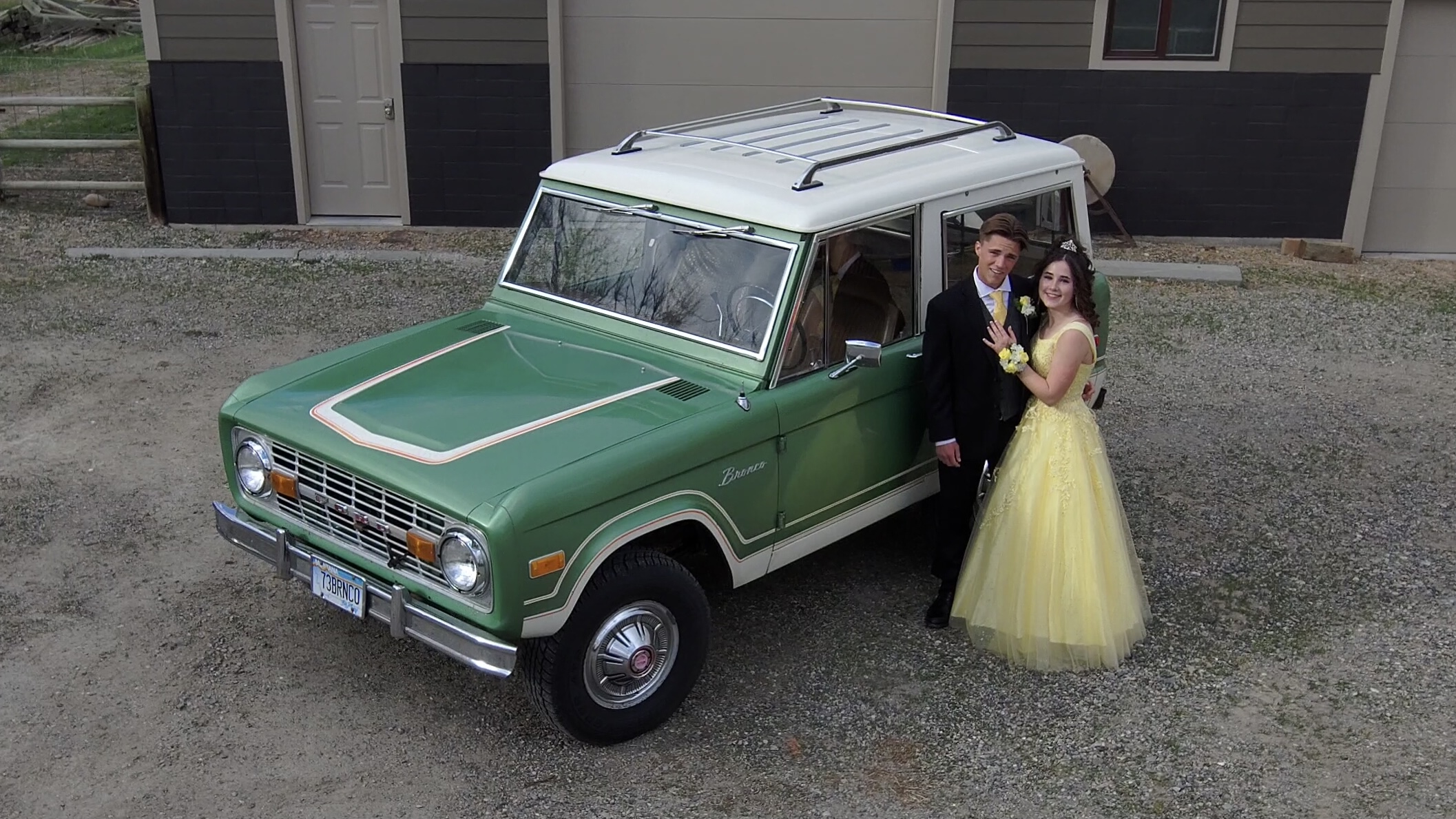 A couple poses in prom attire in front of a green Ford Bronco